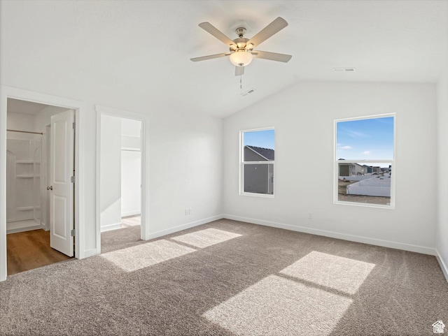 unfurnished bedroom with baseboards, a walk in closet, carpet flooring, and vaulted ceiling