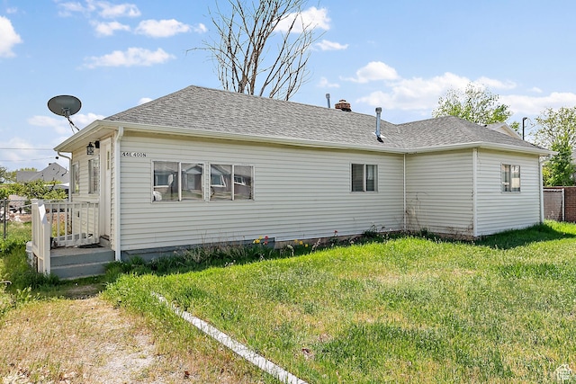 rear view of property featuring a chimney, a yard, and a shingled roof