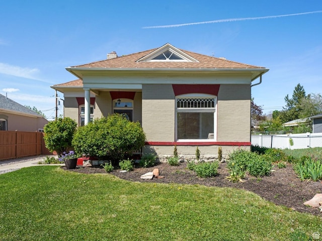 bungalow featuring brick siding, roof with shingles, fence, and a front yard