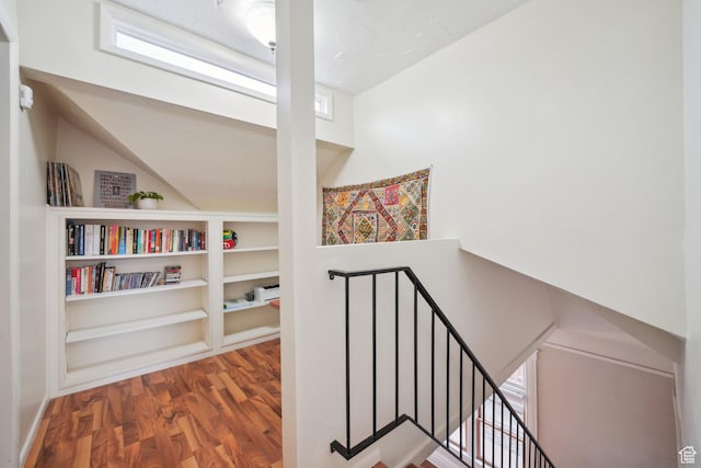 corridor with an upstairs landing, built in shelves, wood finished floors, and lofted ceiling