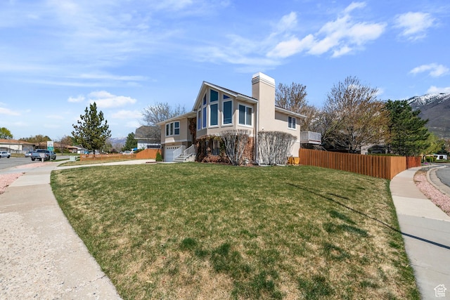 view of side of property featuring a garage, fence, stucco siding, a chimney, and a lawn