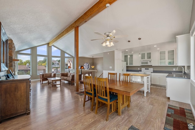 dining space featuring light wood-style floors, baseboards, ceiling fan, and vaulted ceiling with beams