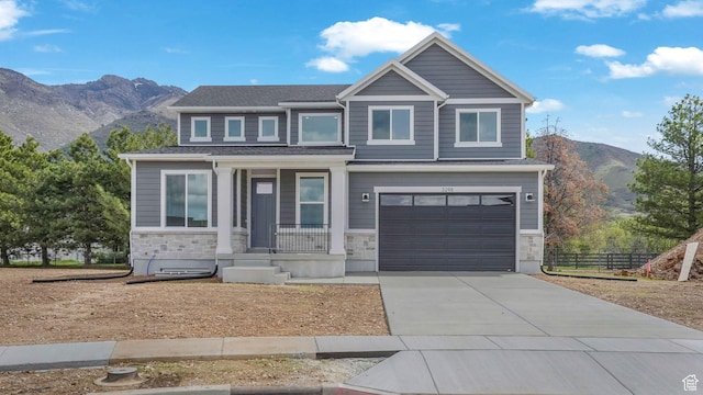 view of front of home featuring a porch, a mountain view, concrete driveway, an attached garage, and stone siding