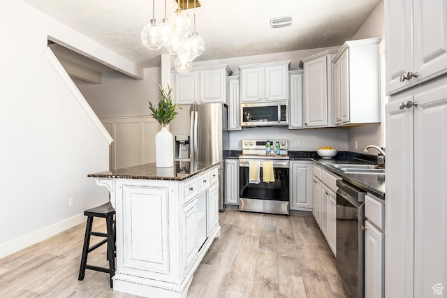 kitchen with a breakfast bar, a sink, light wood-style flooring, stainless steel appliances, and a kitchen island