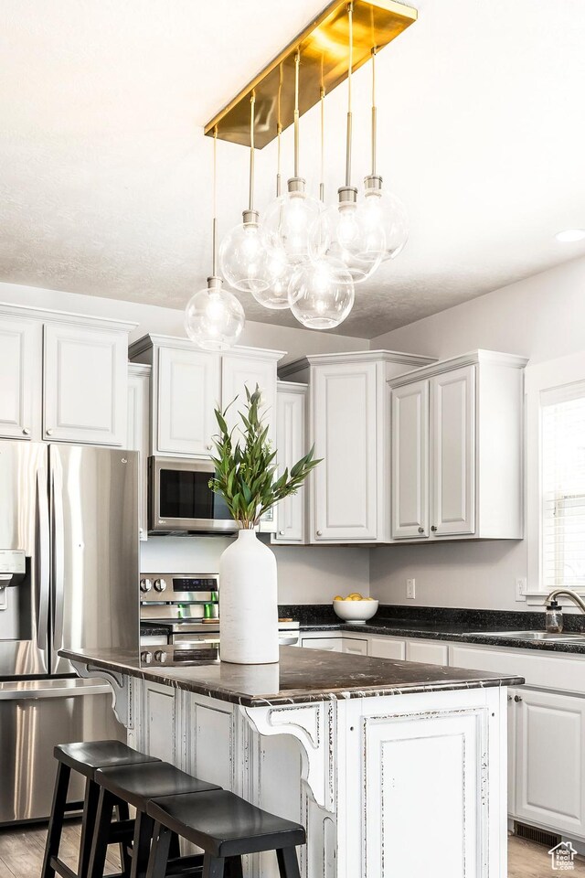 4306 Degray Dr, South Jordan, UT 84095 - kitchen with stainless steel appliances, a kitchen island, a breakfast bar area, decorative light fixtures, and white cabinetry