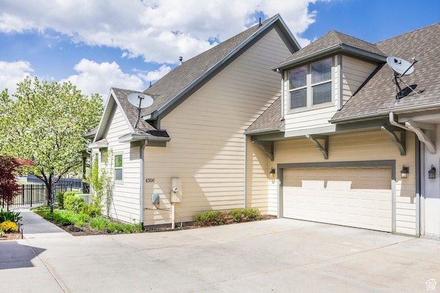 view of side of property featuring fence, a shingled roof, and driveway