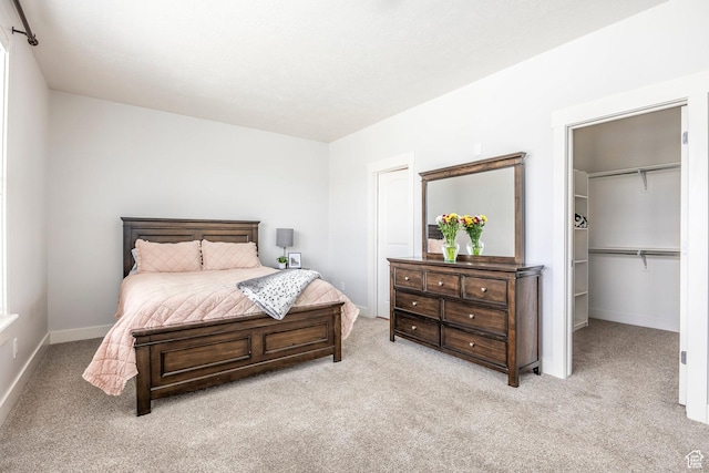 carpeted bedroom featuring baseboards and a walk in closet