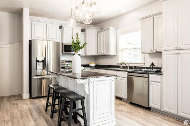 kitchen with a kitchen island, decorative light fixtures, appliances with stainless steel finishes, light wood-type flooring, and a sink