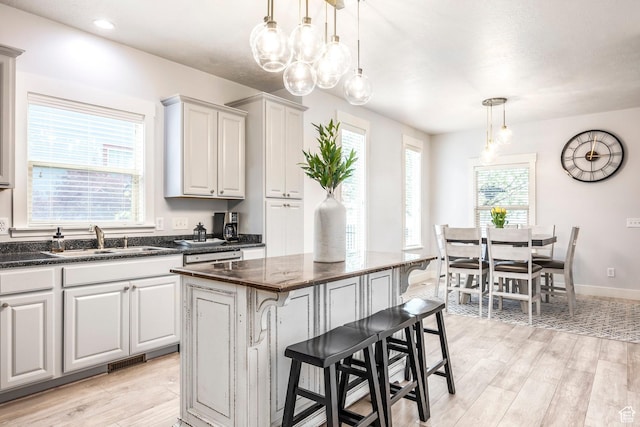 kitchen with a breakfast bar, a sink, decorative light fixtures, light wood-type flooring, and a kitchen island