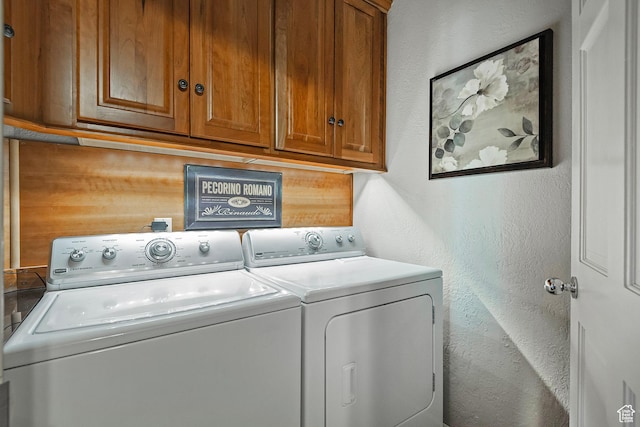 clothes washing area with cabinet space, separate washer and dryer, and a textured wall