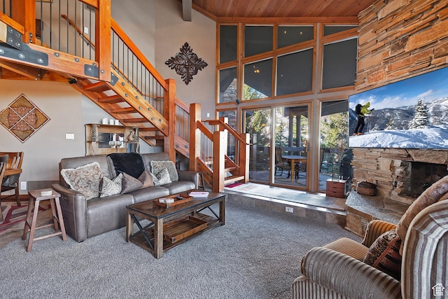 carpeted living room with a stone fireplace, a towering ceiling, stairway, and wooden ceiling