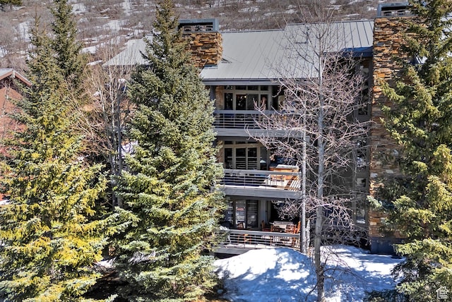 view of front facade featuring a standing seam roof, a balcony, a chimney, and metal roof