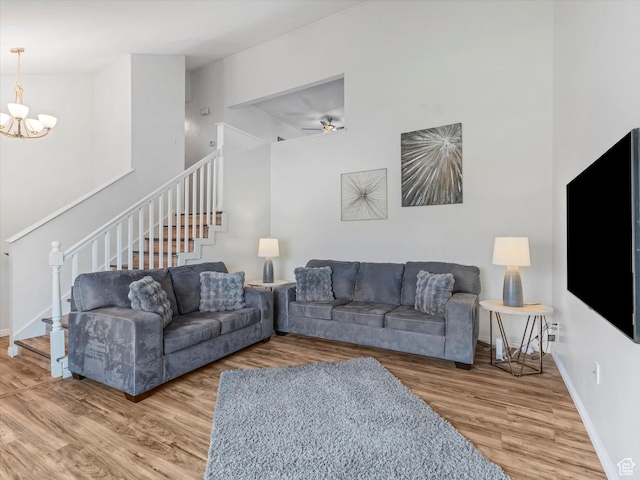 living room featuring baseboards, wood finished floors, stairway, and ceiling fan with notable chandelier