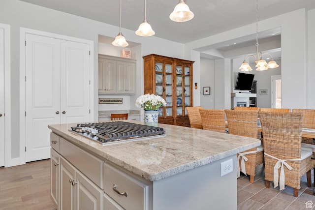 1677 W Escapes Dr Unit 103, St George, UT 84770 - kitchen featuring an inviting chandelier, light stone counters, stainless steel gas cooktop, light wood-style flooring, and a center island