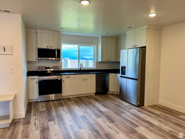 kitchen featuring visible vents, wood finished floors, dark countertops, a sink, and appliances with stainless steel finishes