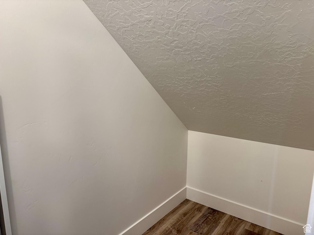 additional living space featuring baseboards, dark wood finished floors, a textured ceiling, and lofted ceiling