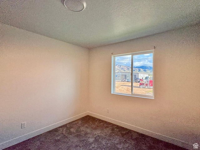 unfurnished room featuring baseboards, dark carpet, and a textured ceiling