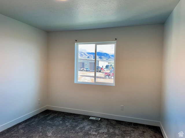 spare room featuring a textured ceiling, baseboards, visible vents, and dark colored carpet