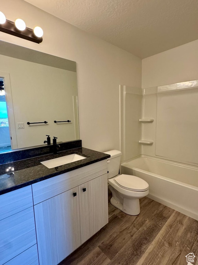 full bathroom with vanity, wood finished floors, toilet, a textured ceiling, and  shower combination