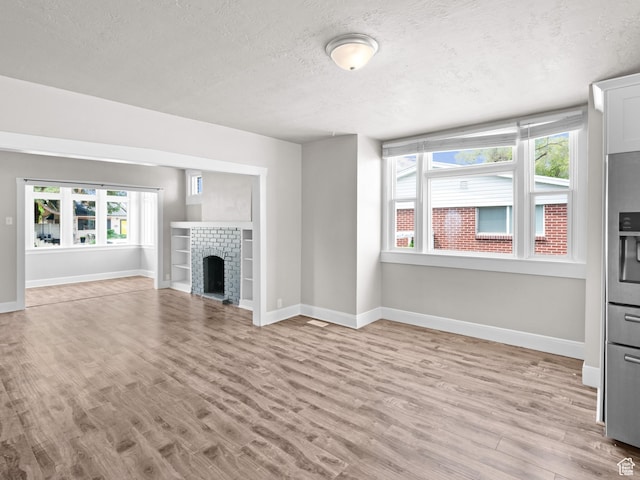 3084 W 3875 S, West Valley City, UT 84119 - unfurnished living room with baseboards, light wood-style flooring, a textured ceiling, and a fireplace