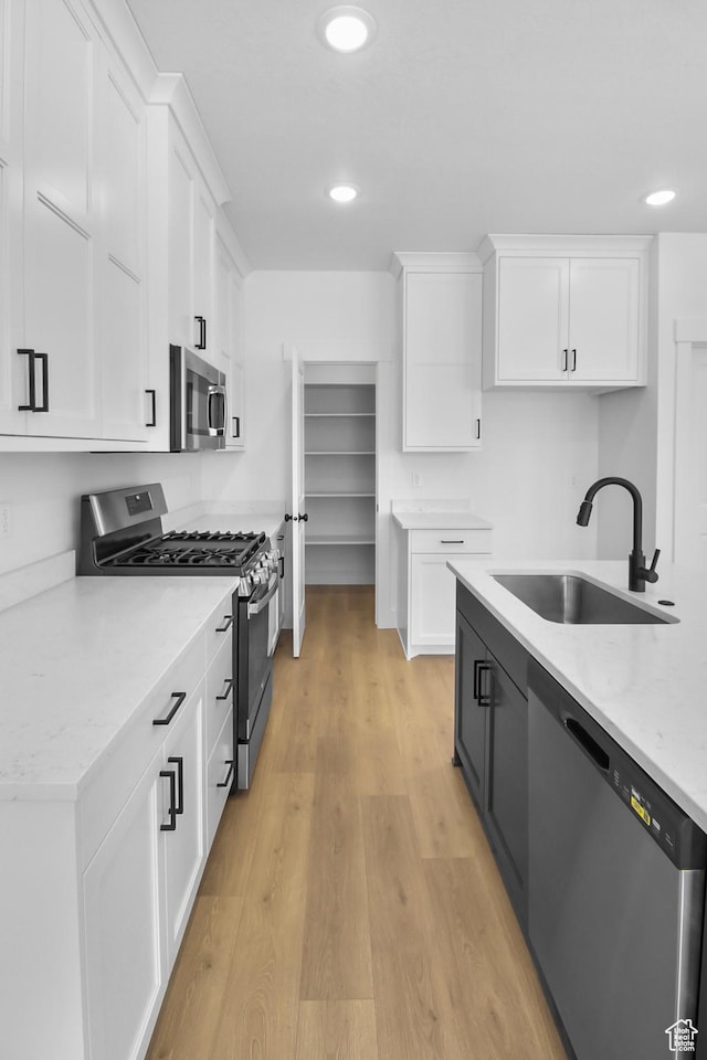 kitchen with white cabinets, appliances with stainless steel finishes, a sink, and light wood-style flooring