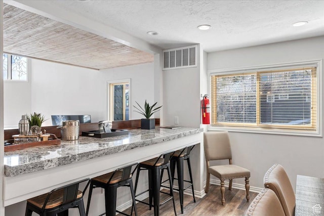 kitchen with light stone counters, baseboards, wood finished floors, a kitchen bar, and visible vents
