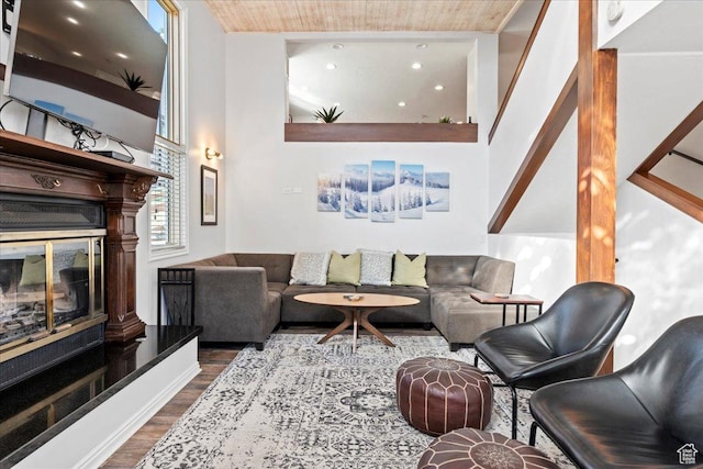 living area featuring dark wood-style flooring, a glass covered fireplace, and wooden ceiling