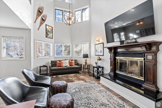living area featuring an inviting chandelier, baseboards, a high ceiling, and wood finished floors
