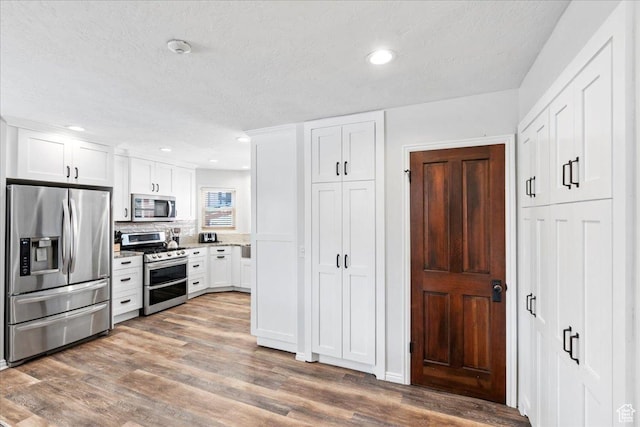 kitchen with a textured ceiling, white cabinetry, appliances with stainless steel finishes, and wood finished floors