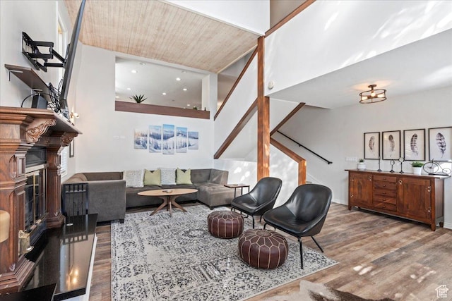 living area with stairs, a fireplace with raised hearth, wooden ceiling, and wood finished floors