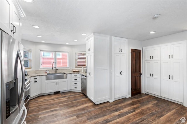 kitchen with a textured ceiling, white cabinetry, light stone counters, a sink, and appliances with stainless steel finishes