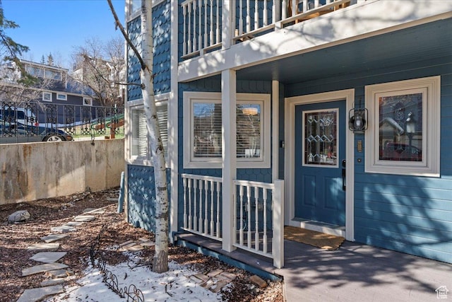 property entrance with a porch, fence, and a balcony