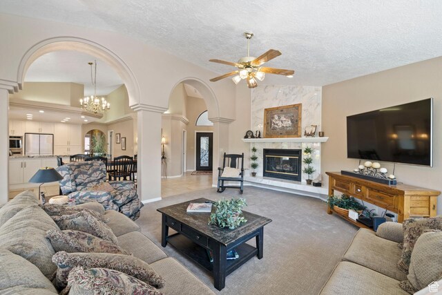 1026 Wesley Powell Dr, St George, UT 84790 - carpeted living area featuring a premium fireplace, arched walkways, a textured ceiling, ceiling fan with notable chandelier, and decorative columns