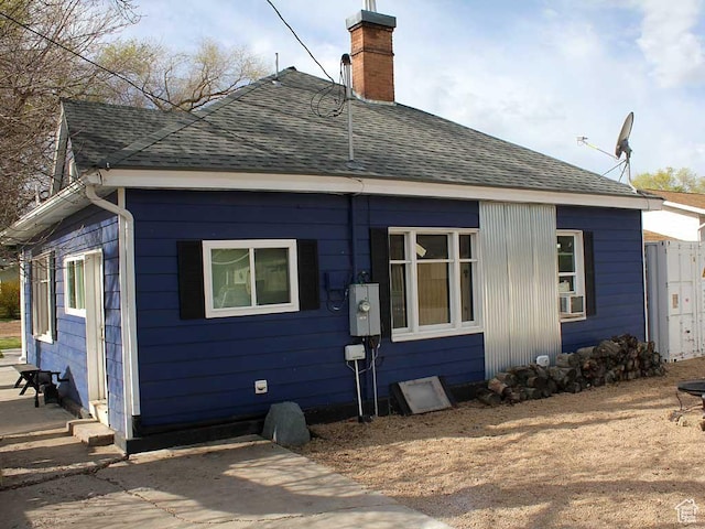 back of house with roof with shingles and a chimney