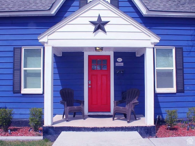 view of exterior entry with a porch and a shingled roof