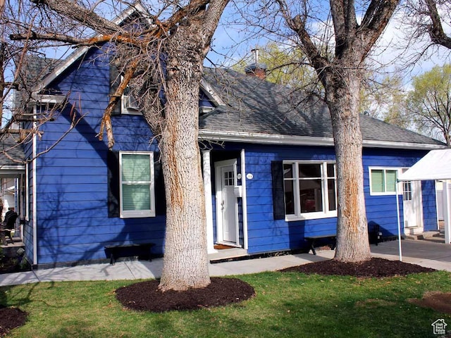 view of front of house with roof with shingles, a front yard, and a chimney