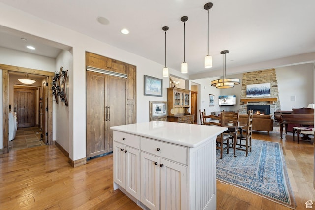 3250 E Thunderhawk Trl, Heber City, UT 84036 - kitchen featuring a center island, hanging light fixtures, a fireplace, white cabinets, and light wood finished floors
