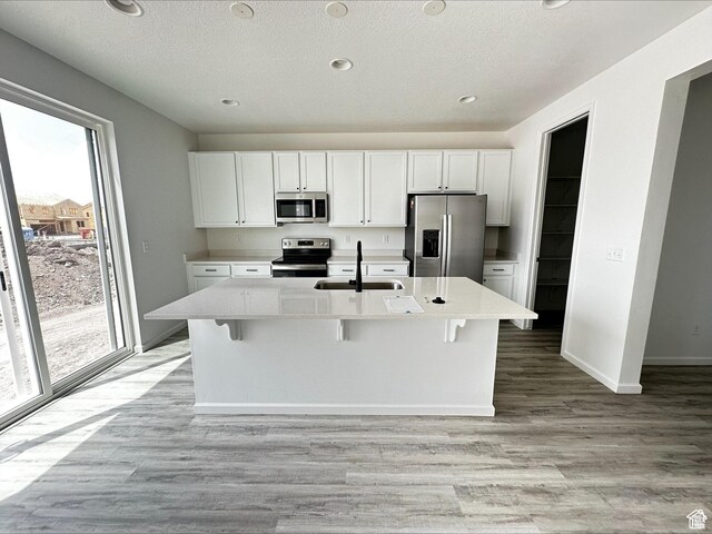 1071 W 400 S Unit 44, Brigham City, UT 84302 - kitchen with stainless steel appliances, a sink, white cabinets, light wood-style flooring, and a kitchen island with sink