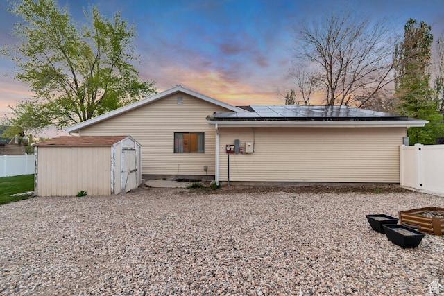 239 Country Club Dr, Stansbury Park, UT 84074 - back of property at dusk with a shed, roof mounted solar panels, fence, and an outdoor structure