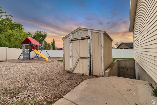 239 Country Club Dr, Stansbury Park, UT 84074 - outdoor structure at dusk featuring a storage unit, a fenced backyard, an outbuilding, and a playground