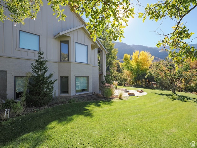 view of side of home featuring board and batten siding, brick siding, a yard, and a mountain view