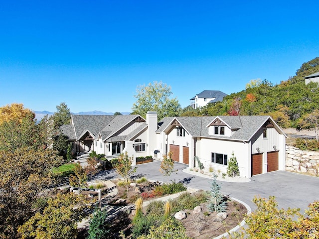 modern inspired farmhouse with an attached garage, aphalt driveway, stucco siding, and a chimney