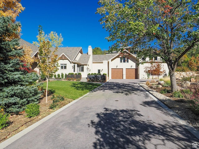 view of front facade with board and batten siding, driveway, a chimney, roof with shingles, and a front lawn