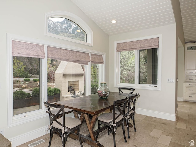 dining room with stone tile floors, baseboards, vaulted ceiling, and visible vents