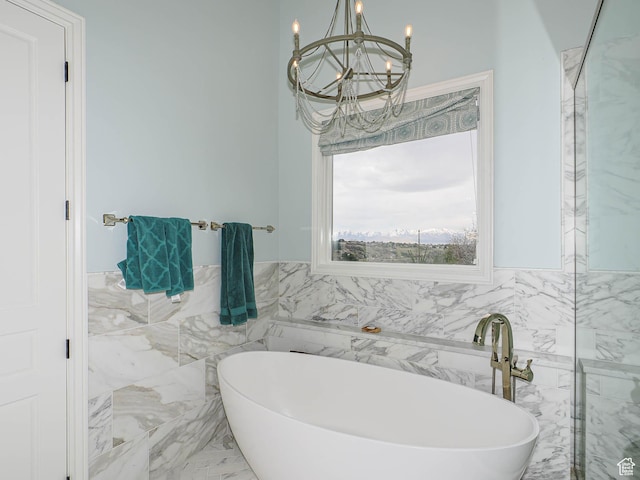 full bathroom featuring tile walls, a wainscoted wall, marble finish floor, an inviting chandelier, and a soaking tub
