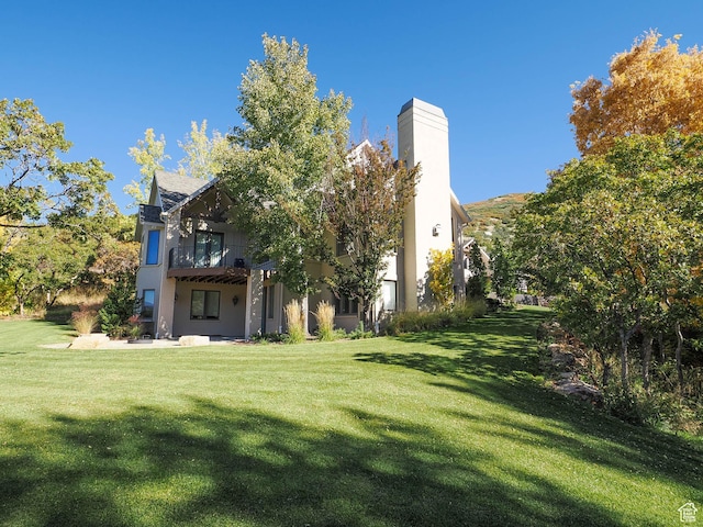 rear view of property featuring a balcony, stucco siding, a yard, and a chimney