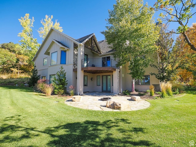 back of house with a balcony, a patio, french doors, board and batten siding, and a lawn