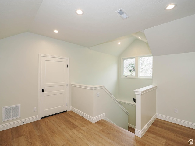 additional living space featuring light wood-style floors, vaulted ceiling, and visible vents