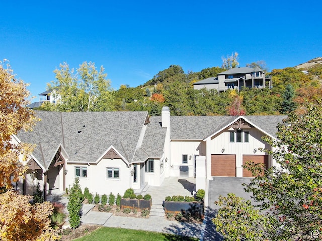 ranch-style home with roof with shingles, a garage, board and batten siding, a chimney, and driveway