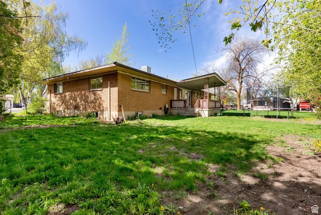 163 E 350 S, Logan, UT 84321 - back of property featuring cooling unit, brick siding, a porch, a trampoline, and a yard